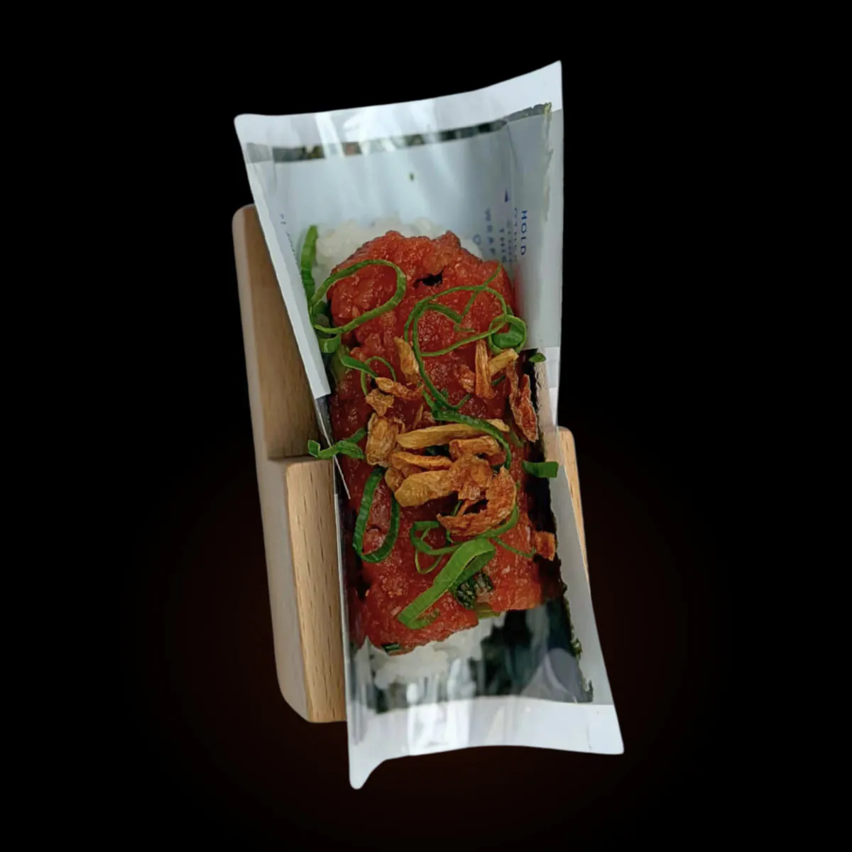 A spicy tuna hand roll with scallion and onion crunch against black